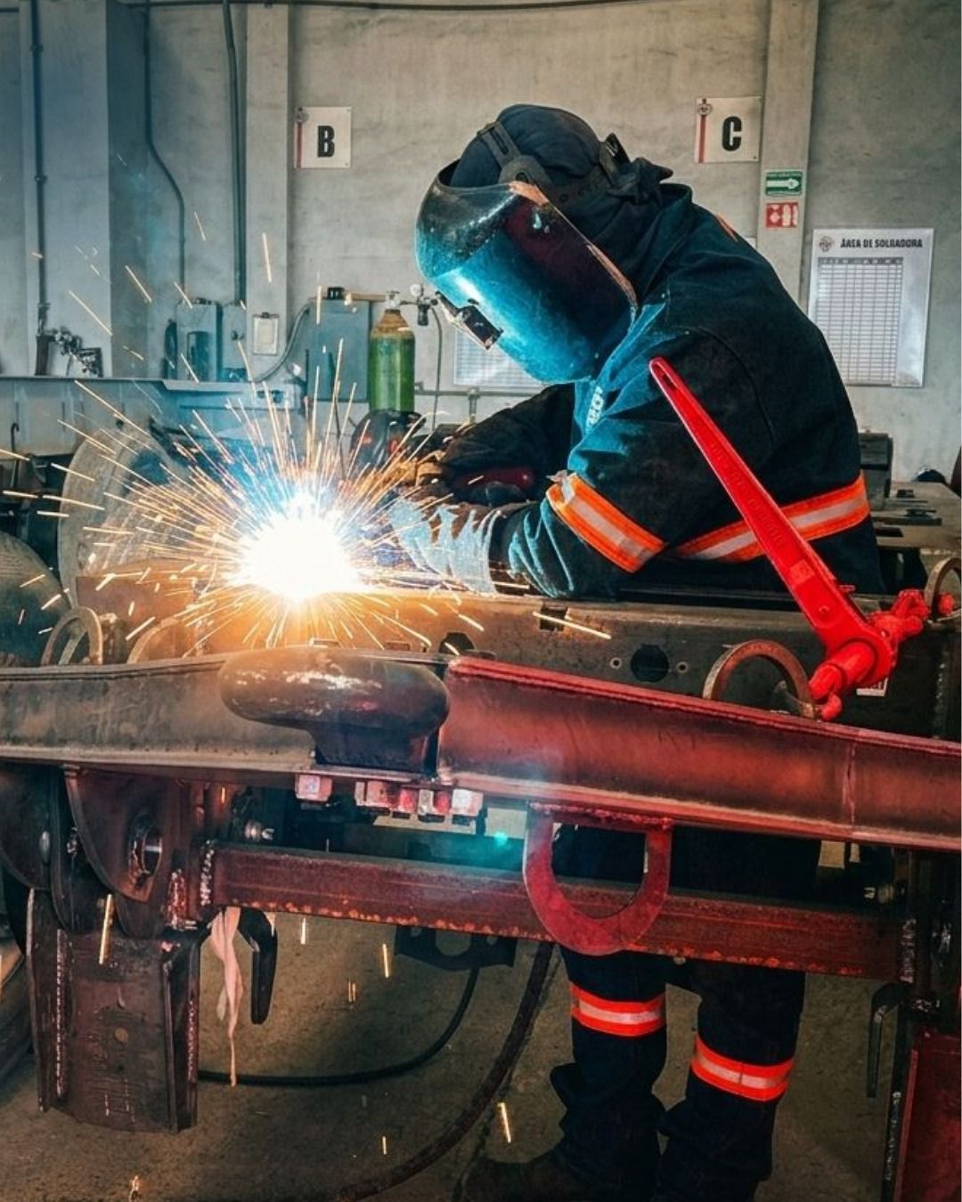 Hombre soldando un remolque portacontenedor en proceso de fabricación industrial en México.